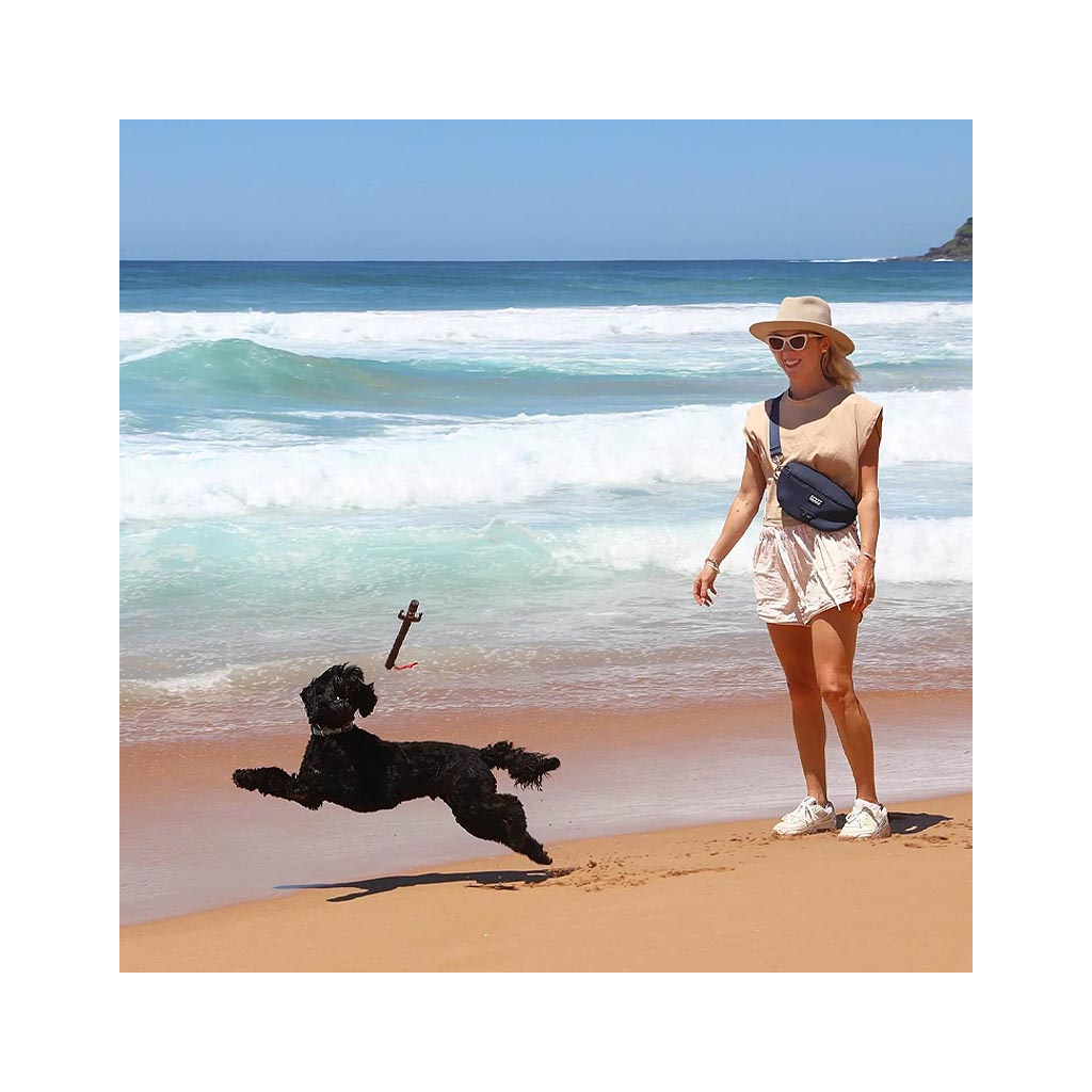 Frau mit DOOG Gürteltasche in Blau spielt am Strand mit ihrem Hund