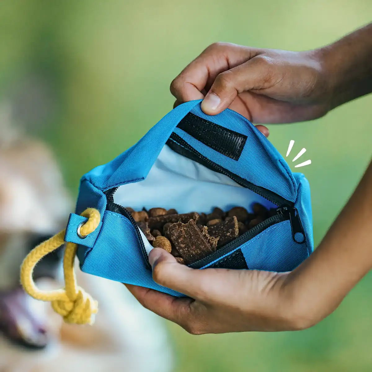 Rudelkönig Leckerlibeutel in Blau, geöffnet mit sichtbarem Inhalt, in der Hand gehalten im Freien.
